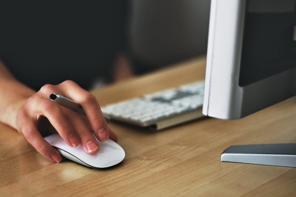 Profissional utiliza o computador. Vemos em destaque sua mão no mouse. (Foto: Vojtech Okenka/Pexels).