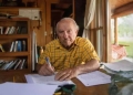 Imagem de Yvon Chouinard, bilionário que doou fortuna, sentado à mesa.