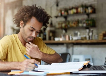 Homem negro, de camisa amarela, estudando.