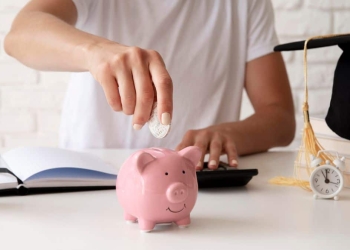 Pessoa depositando moeda em cofrinho de porquinho rosa, simbolizando economia.