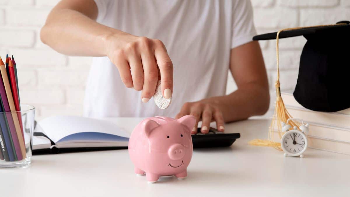 Pessoa depositando moeda em cofrinho de porquinho rosa, simbolizando economia.