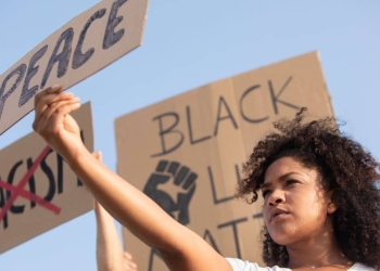 Mulher negra segura um cartaz escrito "Peace" em protesto pela igualdade racial e resistência negra.