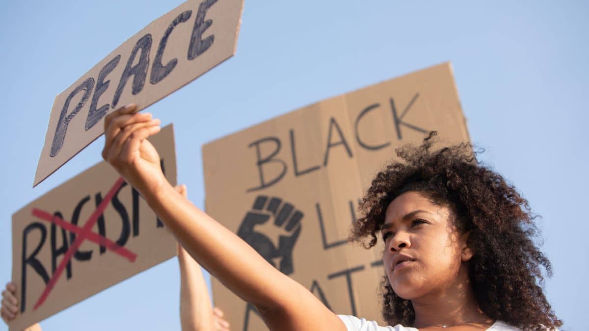 Mulher negra segura um cartaz escrito "Peace" em protesto pela igualdade racial e resistência negra.