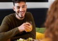 Homem feliz comendo enquanto toma uma bebida.