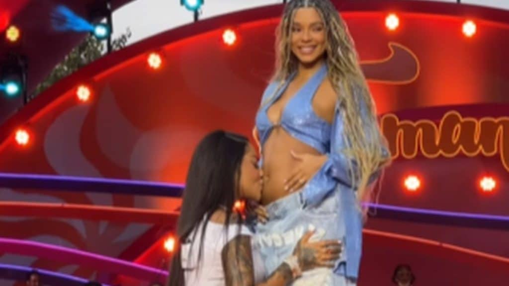 Cantora Ludmilla ajoelhada e beijando a barriga da esposa Brunna.