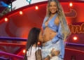 Cantora Ludmilla ajoelhada e beijando a barriga da esposa Brunna.