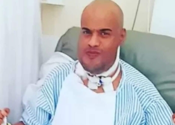 Thiago dos Reis vestido com roupa hospitalar após cirurgia de retirada da língua.