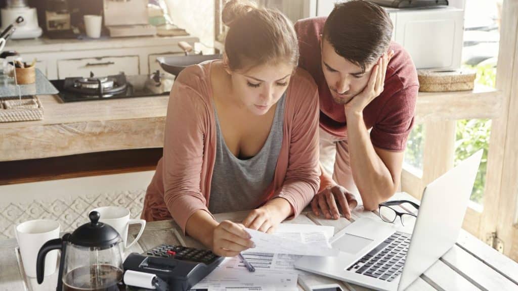 Casal revisa orçamento familiar com calculadora e laptop.