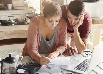 Casal revisa orçamento familiar com calculadora e laptop.