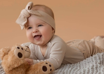 Imagem de um bebê sorrindo, deitado em uma manta com um ursinho de pelúcia.