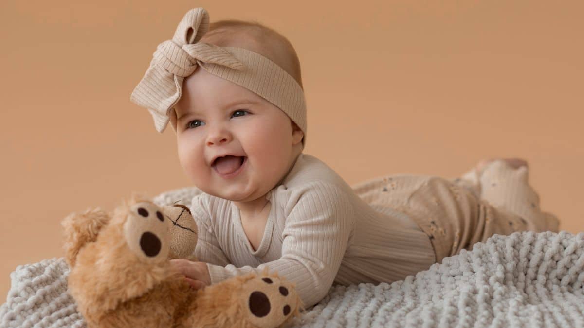 Imagem de um bebê sorrindo, deitado em uma manta com um ursinho de pelúcia.