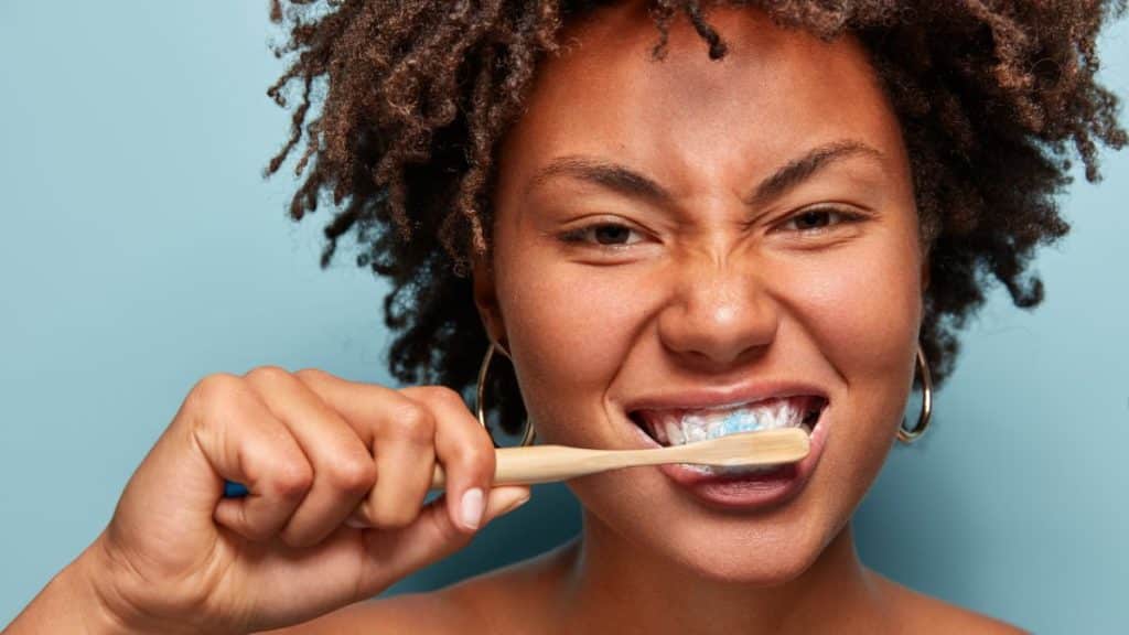 Mulher sorridente escovando os dentes com uma escova de bambu.