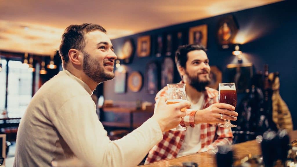 Imagens de dois homens brancos bebendo em um bar.