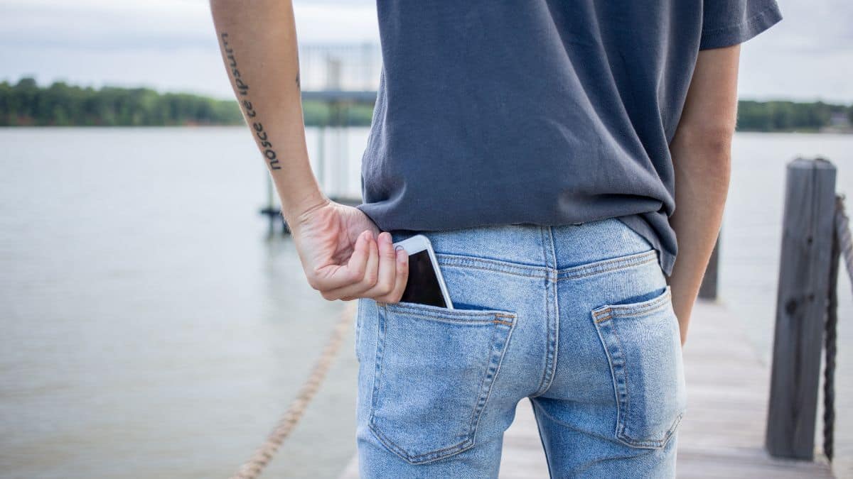 Homem com celular no bolso de trás da calça, em imagem ilustrativa.