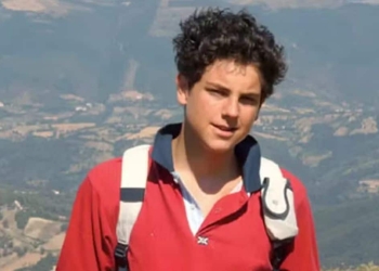 Fotografia de Carlo Acutis, adolescente italiano com uma mochila, em um cenário de paisagem montanhosa. Carlo é conhecido como o "padroeiro da internet" e será canonizado em 2025.