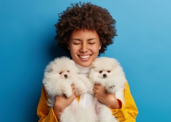 Imagem de uma jovem negra carregando dois cachorros pequenos e brancos.