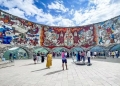 Vista do Monumento à Amizade Rússia-Geórgia, com seu colorido mosaico que retrata cenas históricas e culturais, emoldurado pelas montanhas do Cáucaso.