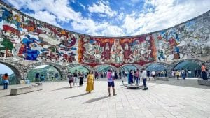 Vista do Monumento à Amizade Rússia-Geórgia, com seu colorido mosaico que retrata cenas históricas e culturais, emoldurado pelas montanhas do Cáucaso.