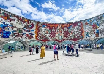 Vista do Monumento à Amizade Rússia-Geórgia, com seu colorido mosaico que retrata cenas históricas e culturais, emoldurado pelas montanhas do Cáucaso.