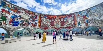 Vista do Monumento à Amizade Rússia-Geórgia, com seu colorido mosaico que retrata cenas históricas e culturais, emoldurado pelas montanhas do Cáucaso.