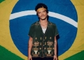 Cantor Bruno Mars parado na frente de uma bandeira do Brasil pintada na parede.