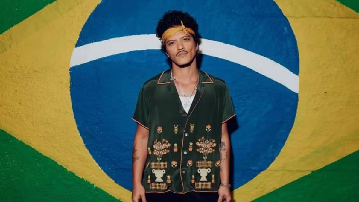 Cantor Bruno Mars parado na frente de uma bandeira do Brasil pintada na parede.