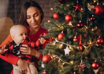 Mulher segurando bebê ao lado da árvore de natal.