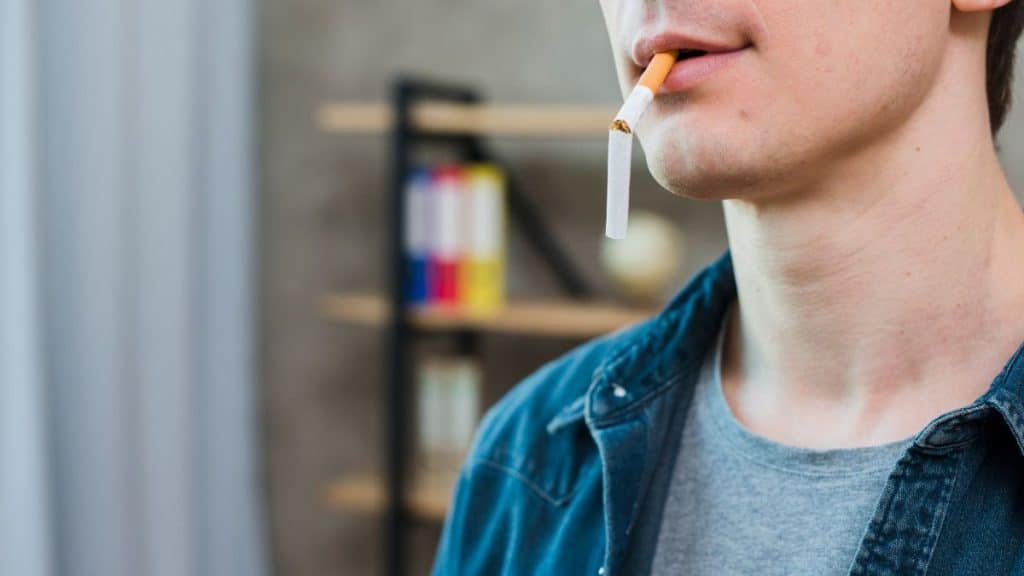 Imagem de um homem com cigarro quebrado na boca.