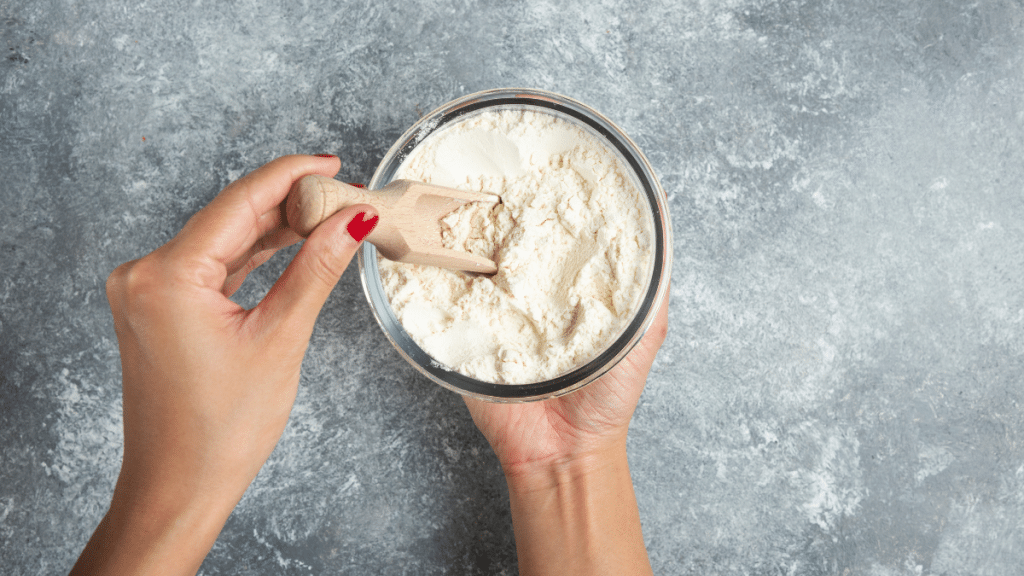 Mão segurando um recipiente com whey protein em pó, mostrando sua versatilidade como suplemento alimentar.