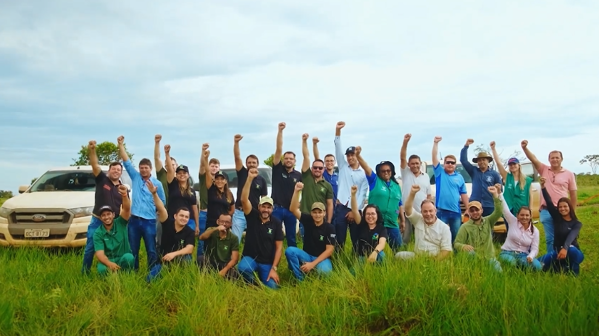 Equipe do Grupo RZK e parceiros em uma área verde, comemorando com os braços erguidos, destacando união e ações de sustentabilidade ambiental.