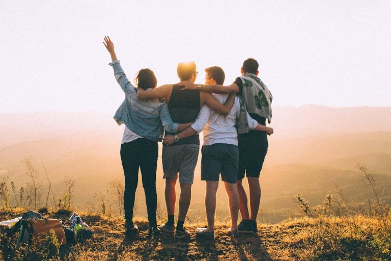 Grupo de amigos abraçados ao pôr do sol, simbolizando união, amizade e sinceridade nos relacionamentos.