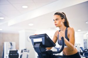 Mulher treinando em academia em uma bicicleta ergométrica, focada em alcançar seu objetivo na atividade física.