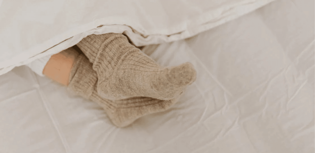 Pessoa dormindo com meia de lã sob cobertor, representando o uso de meias para melhorar a qualidade do sono.