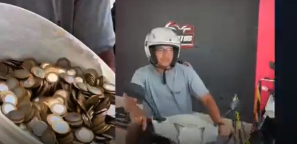 Balde cheio de moedas ao lado de um jovem usando capacete, sentado em uma moto dentro de uma loja de revenda de veículos.