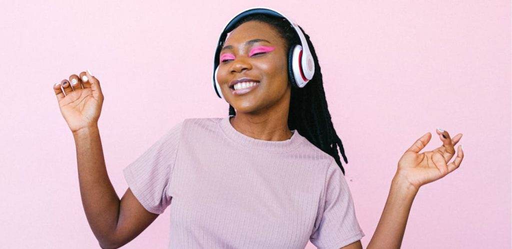 Mulher sorridente ouvindo música com fones de ouvido, demonstrando bem-estar e relaxamento. A música pode ajudar a aliviar o estresse e a ansiedade