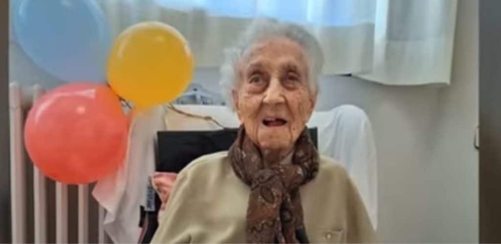 Maria Branyas Morera, uma supercentenária de 117 anos, sorri enquanto comemora sua longevidade. A idosa, reconhecida pelo Guinness World Records, viveu com lucidez até o fim da vida. Ao fundo, balões coloridos decoram o ambiente, simbolizando a celebração de uma vida longa e saudável.