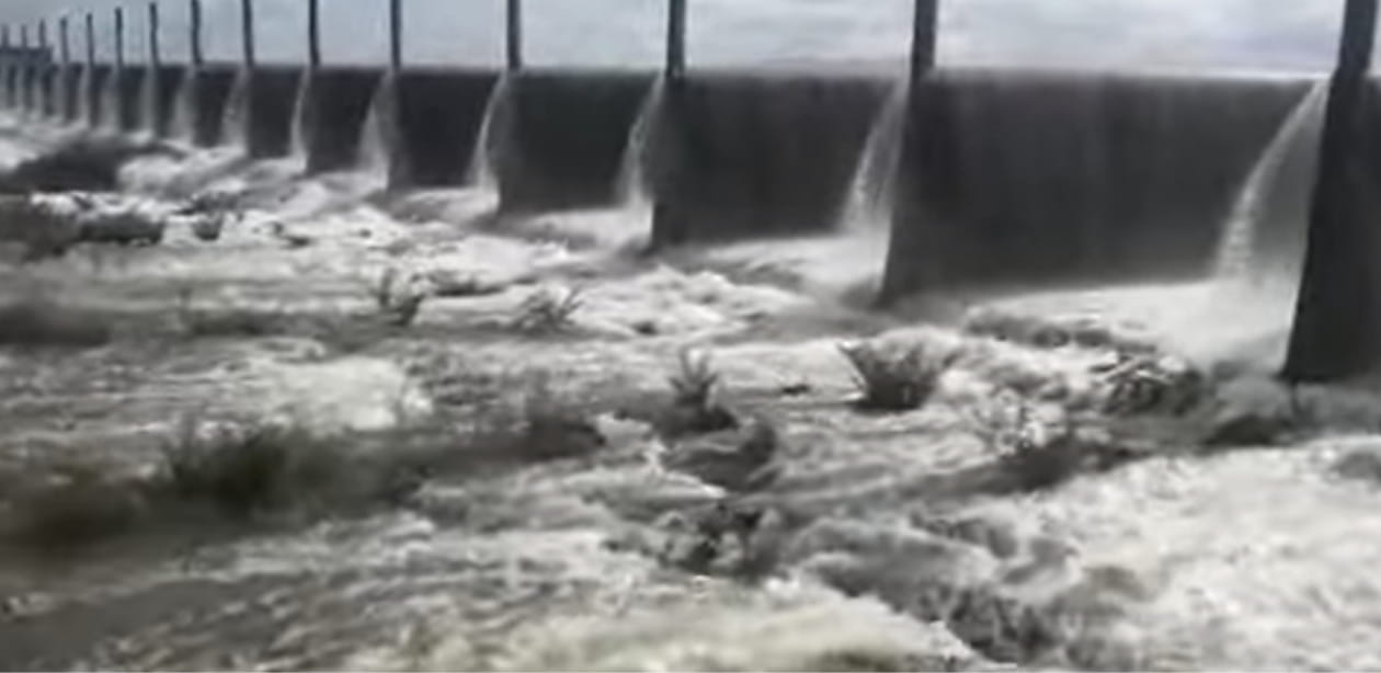 Imagem do Açude Pacajus transbordando, com fortes correntes de água escoando sobre a barragem. O volume intenso reflete o impacto das chuvas na região, contribuindo para a recarga dos reservatórios no Ceará