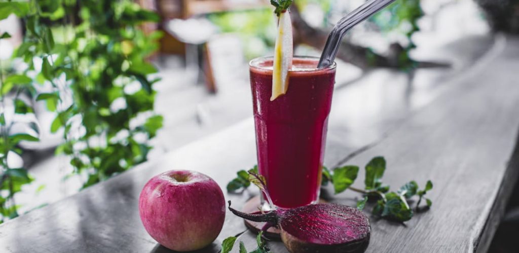 Copo de suco de beterraba ao lado de uma maçã e uma beterraba cortada, destacando os benefícios do suco para desempenho físico e recuperação muscular