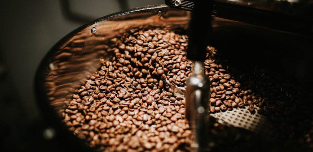 Grãos de café torrados em um equipamento de torrefação, destacando o brilho e a textura dos grãos prontos para moagem e preparo