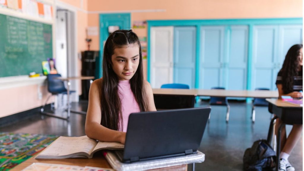 Estudante em sala de aula usando um laptop para aprender sobre inteligência artificial no currículo escolar, destacando o uso da tecnologia na educação.