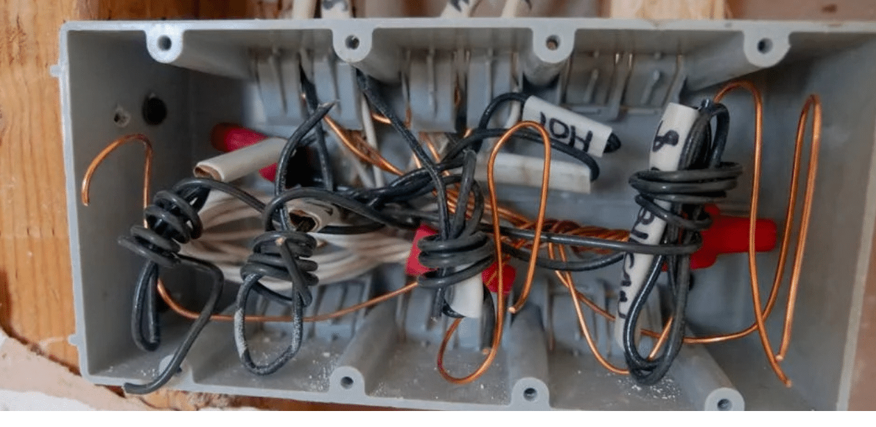 Fiação elétrica desorganizada dentro de caixa de passagem, representando risco de descarga elétrica residencial