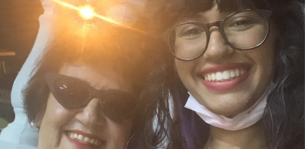 Idosa e jovem sorrindo juntas em casa intergeracional, representando convivência entre gerações e combate à solidão