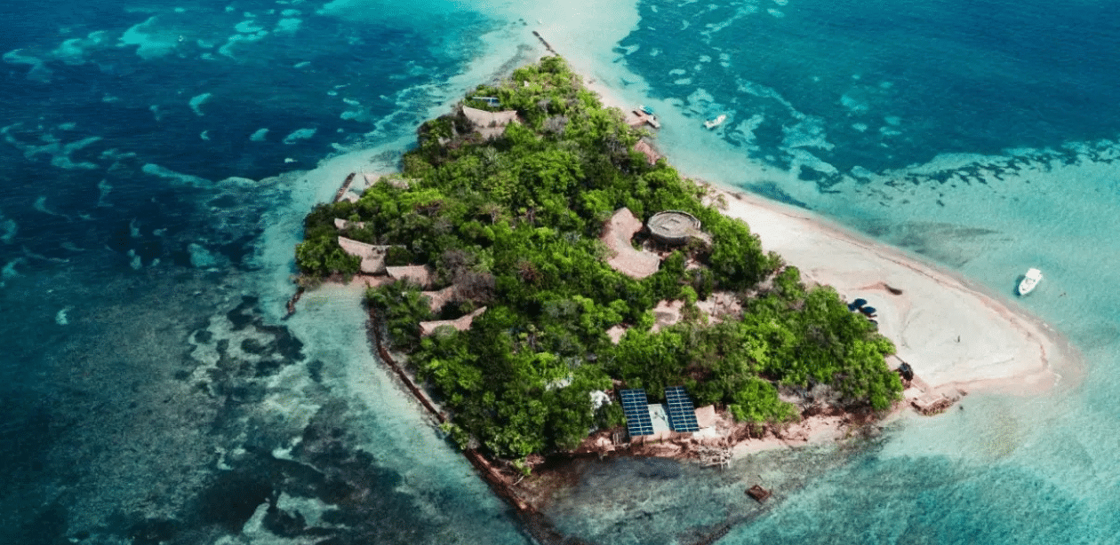 Imagem aérea da Ilha Corona na Colômbia, cercada por águas cristalinas do Caribe, com bangalôs sustentáveis em meio à vegetação.