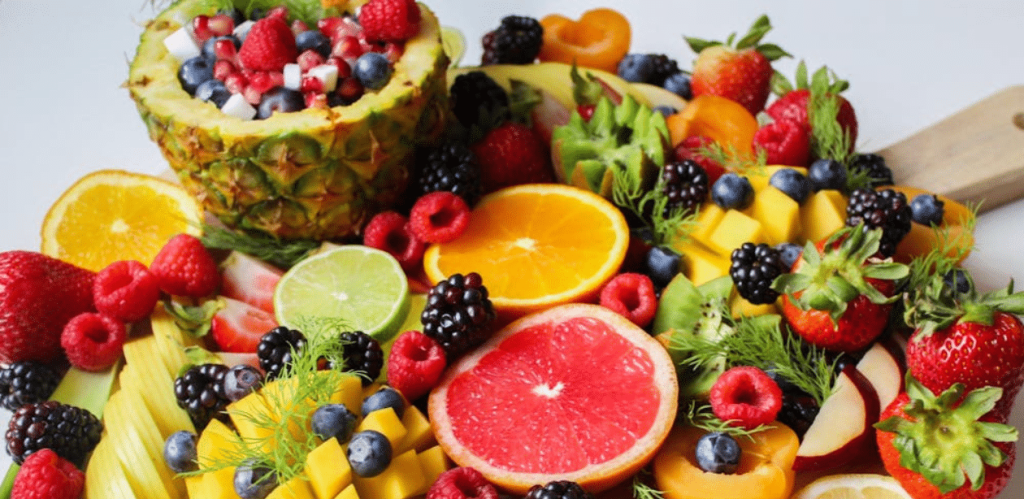 Variedade colorida de frutas ricas em fibras, como morango, laranja, framboesa, kiwi e abacaxi, dispostas sobre uma tábua.
