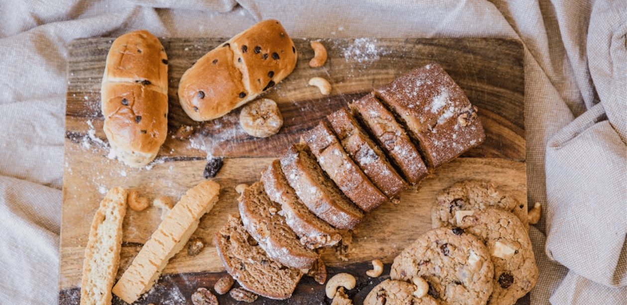 Pães, biscoitos e bolos sobre tábua de madeira, alimentos ricos em carboidratos consumidos com moderação em dietas equilibradas