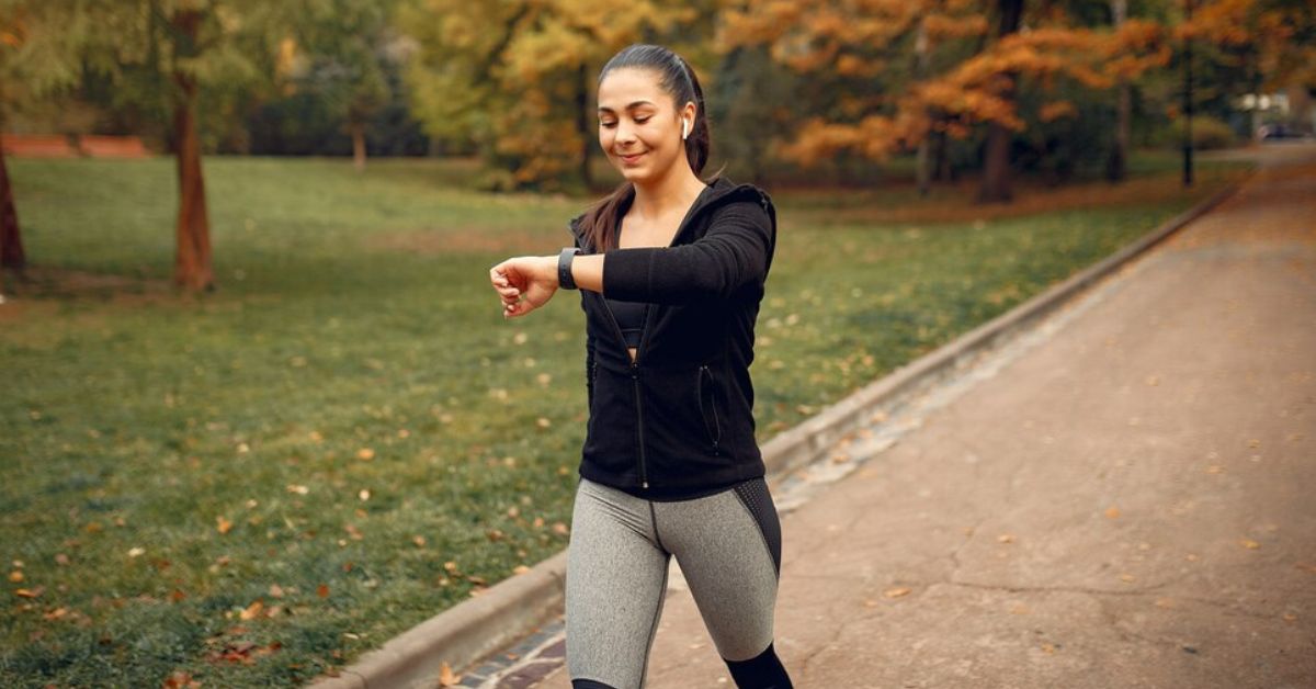 Mulher praticando caminhada para emagrecer em parque arborizado, mantendo ritmo acelerado e monitorando o tempo no relógio