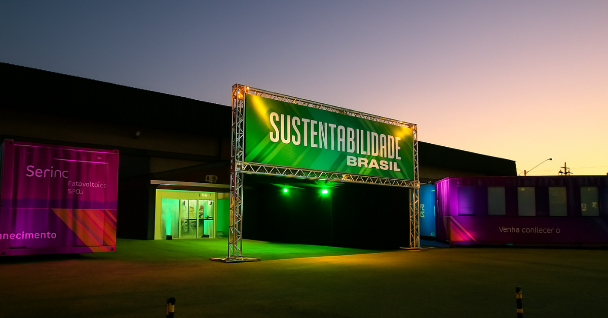 Entrada iluminada do Evento Sustentabilidade Brasil com estrutura metálica e painel verde ao entardecer