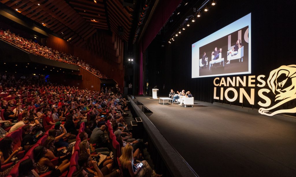 Foto do Festival Internacional de Criatividade de Cannes, mostrando uma plateia entusiasmada durante uma das palestras sobre inovação e criatividade no setor publicitário.