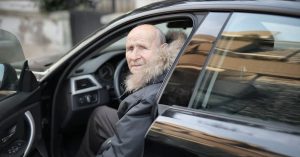 Idoso sentado ao volante simboliza o desconto para idosos na compra de carro.