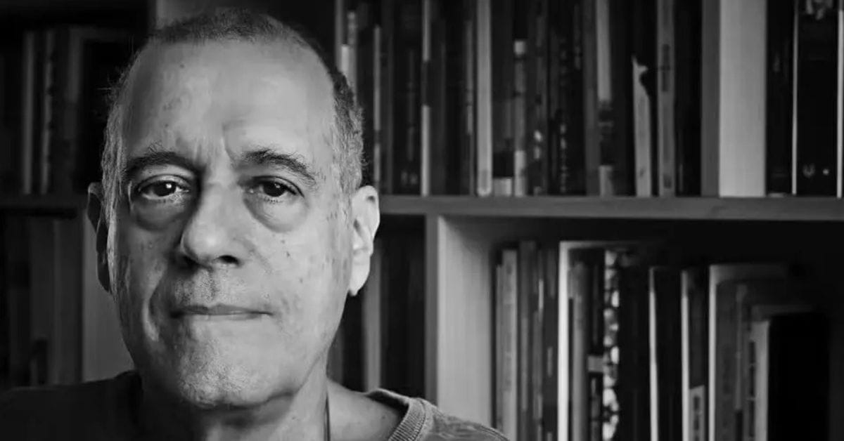 Paulo Henriques Britto diante de estante de livros, em retrato em preto e branco